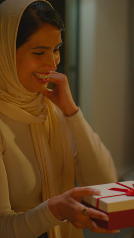 Vertical-Video-Of-Woman-Wearing-Hijab-Receiving-Birthday-Present-At-Home-With-Party-Balloons-In-Background